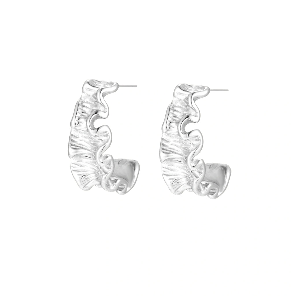 White gold plated sculptural hoop earrings with organic wavy edges and reflective metallic finish on cream background