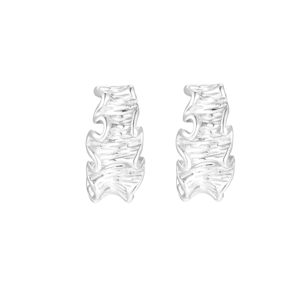 White gold plated sculptural hoop earrings with organic wavy edges and reflective metallic finish on cream background