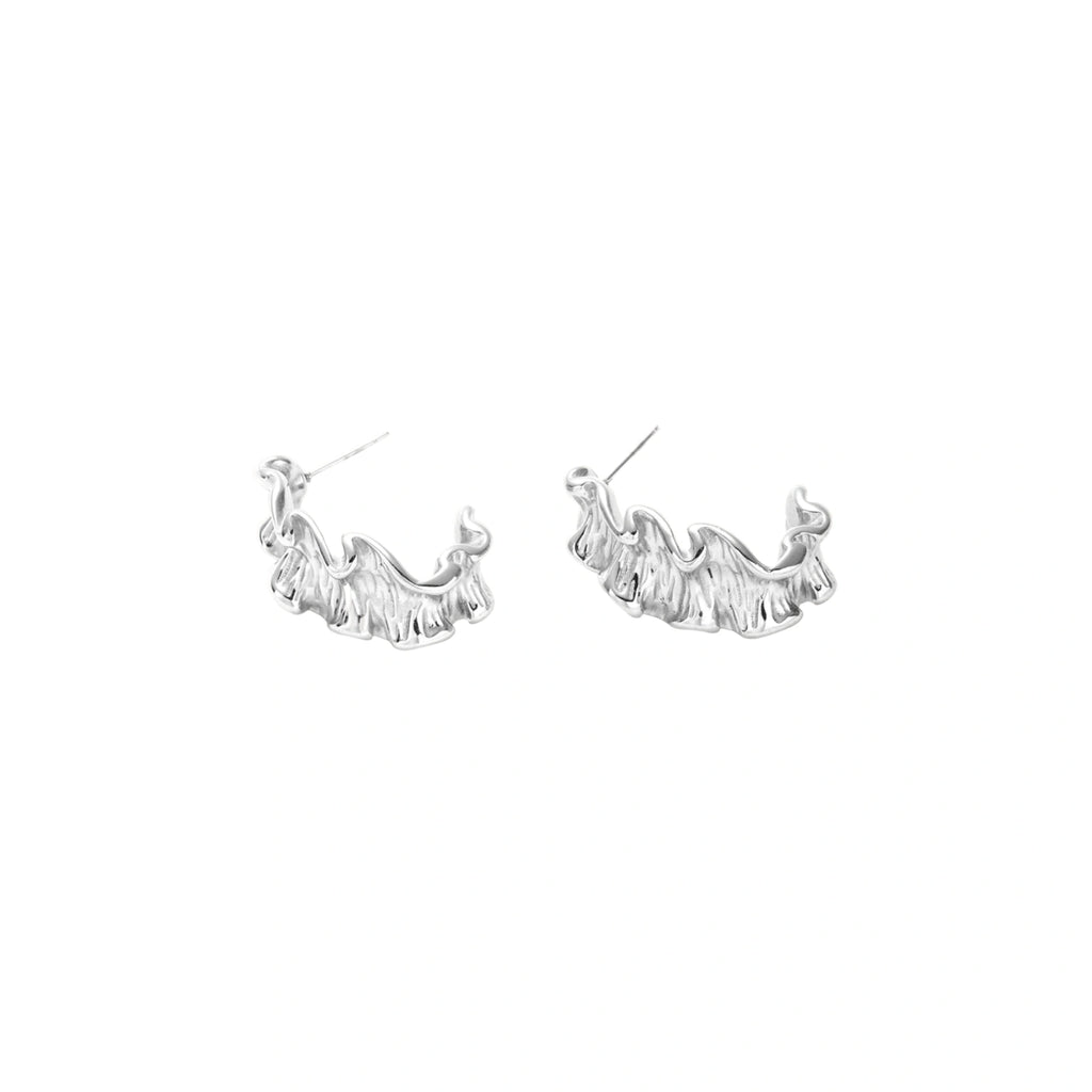 White gold plated sculptural hoop earrings with organic wavy edges and reflective metallic finish on cream background