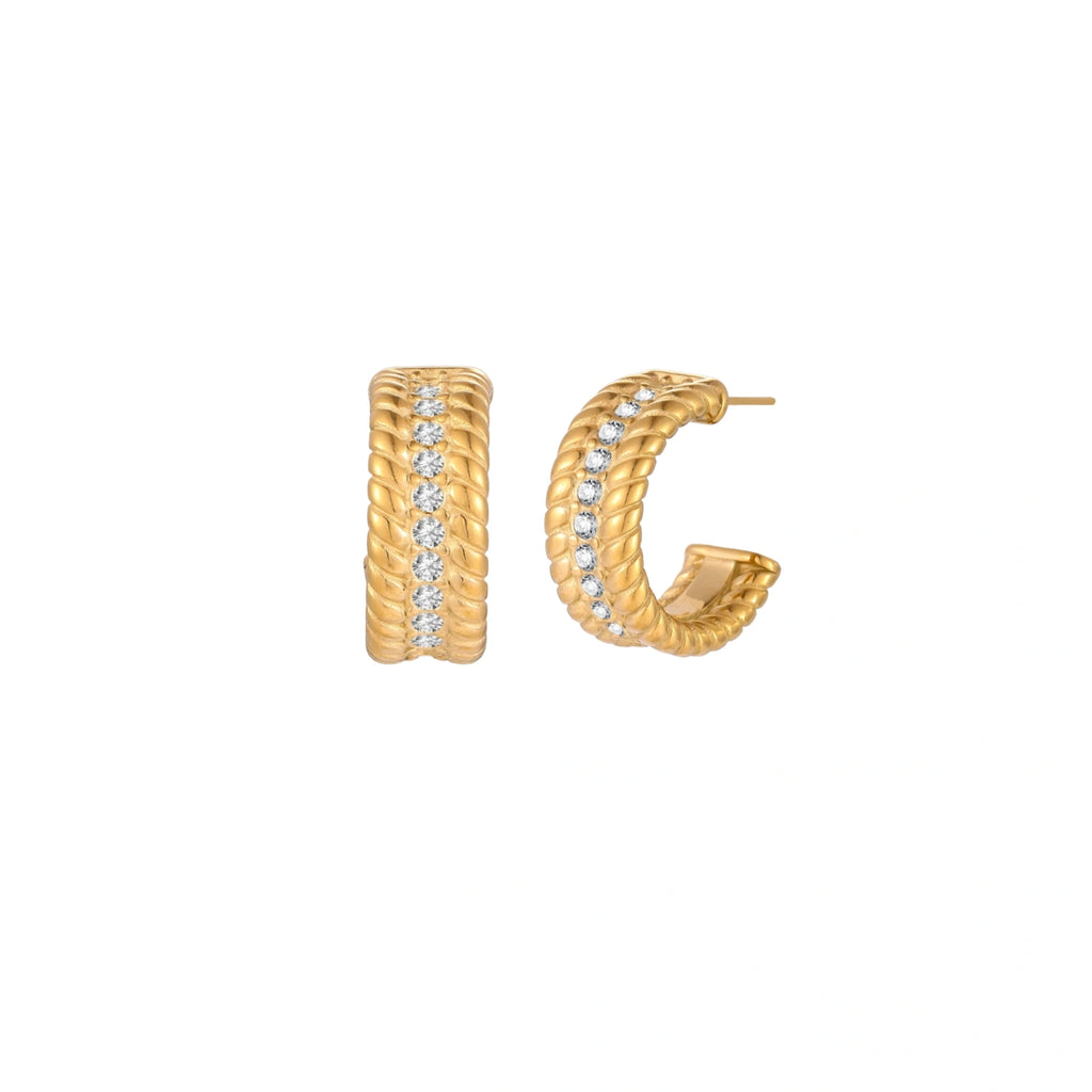 Textured gold huggie hoop earrings with raised ribbed rows creating dimensional sculptural design on cream background