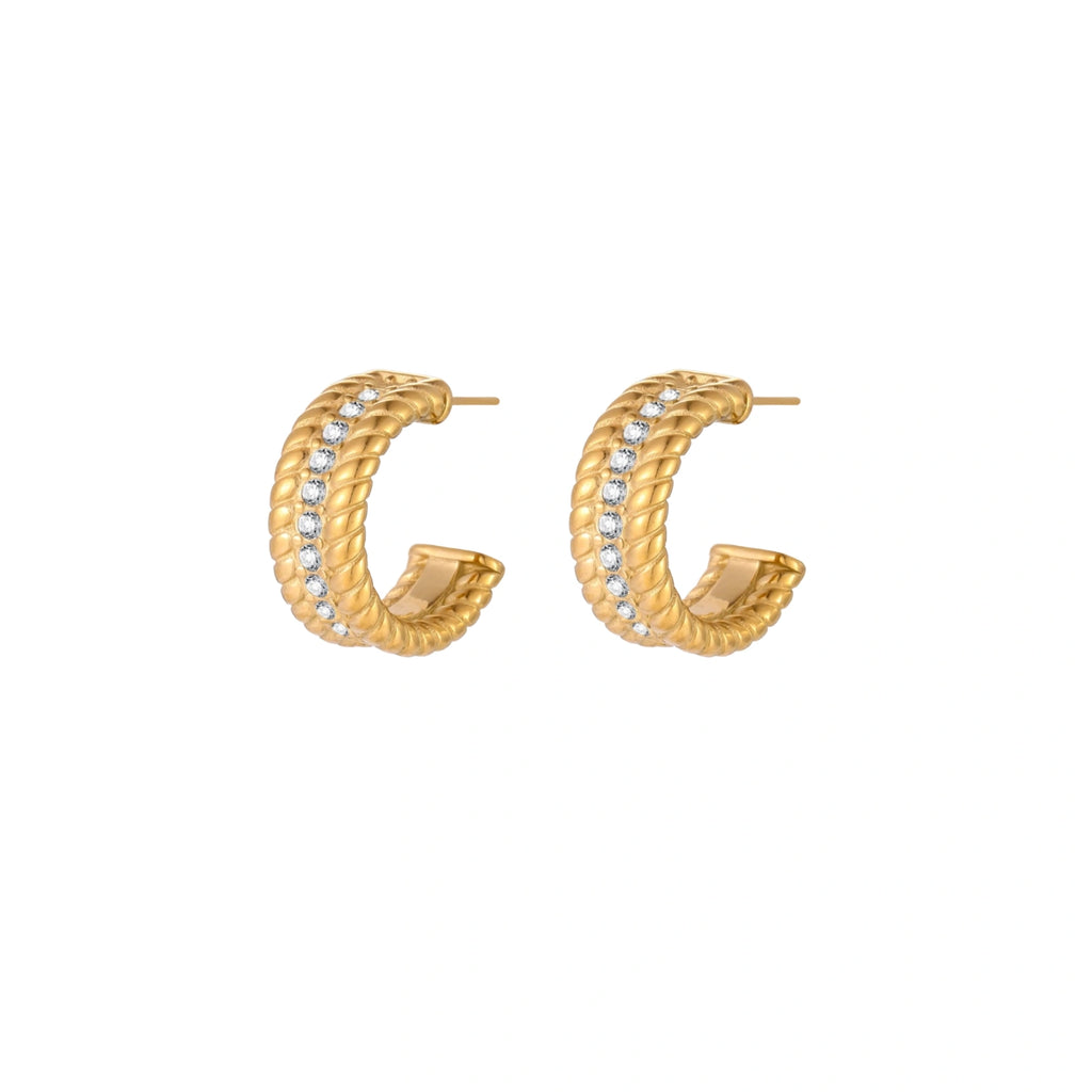 Textured gold huggie hoop earrings with raised ribbed rows creating dimensional sculptural design on cream background