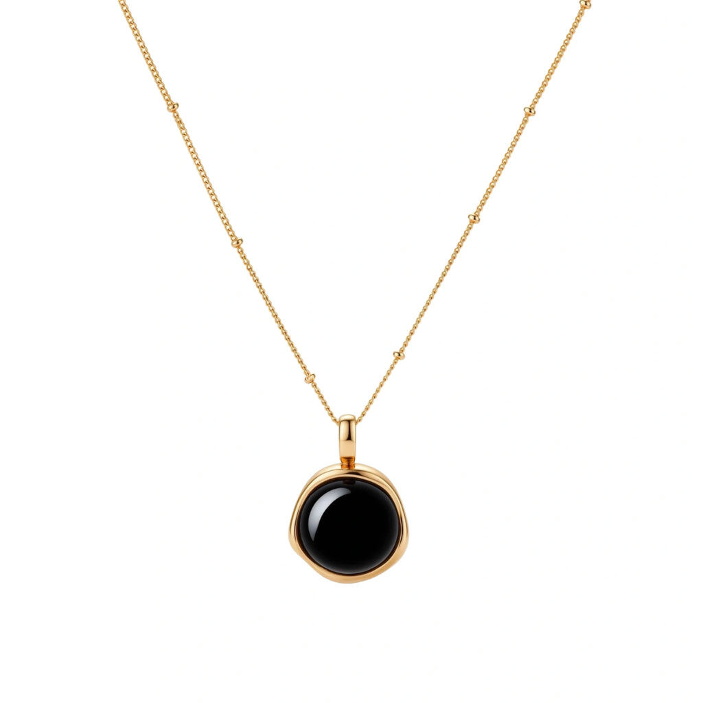 Circular black agate pendant on gold-plated sterling silver chain against cream background, showing modern minimalist design.