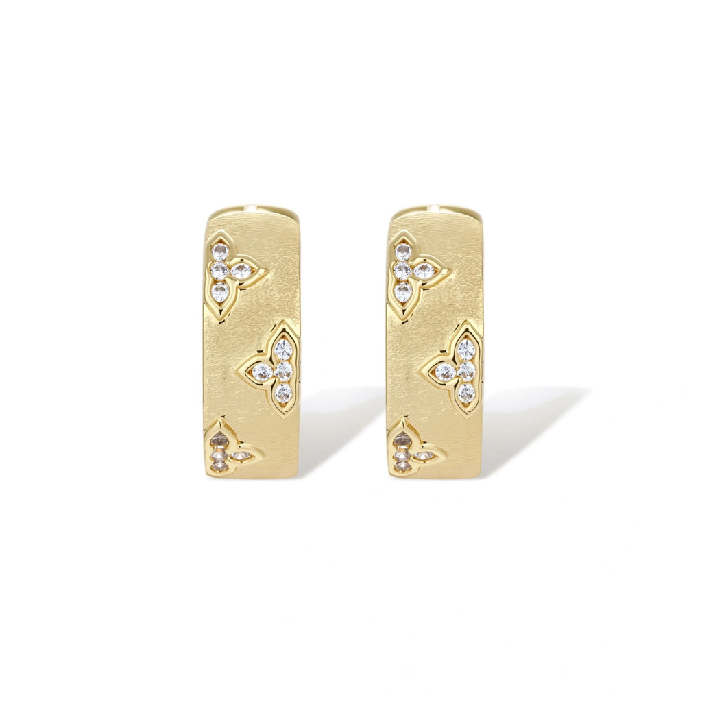 Gold-plated hoop earrings with textured surface and raised floral motifs set with clear zirconia stones on cream background.